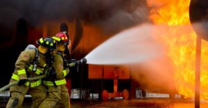 two firemen spraying water to put out huge fire