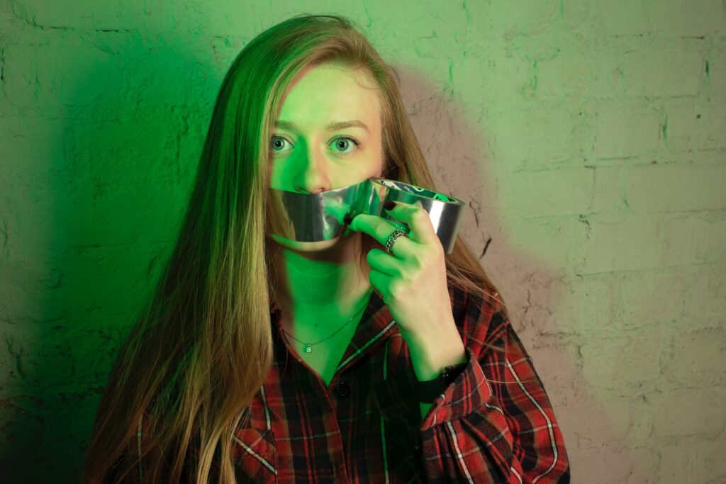 A woman putting duct tape over her mouth